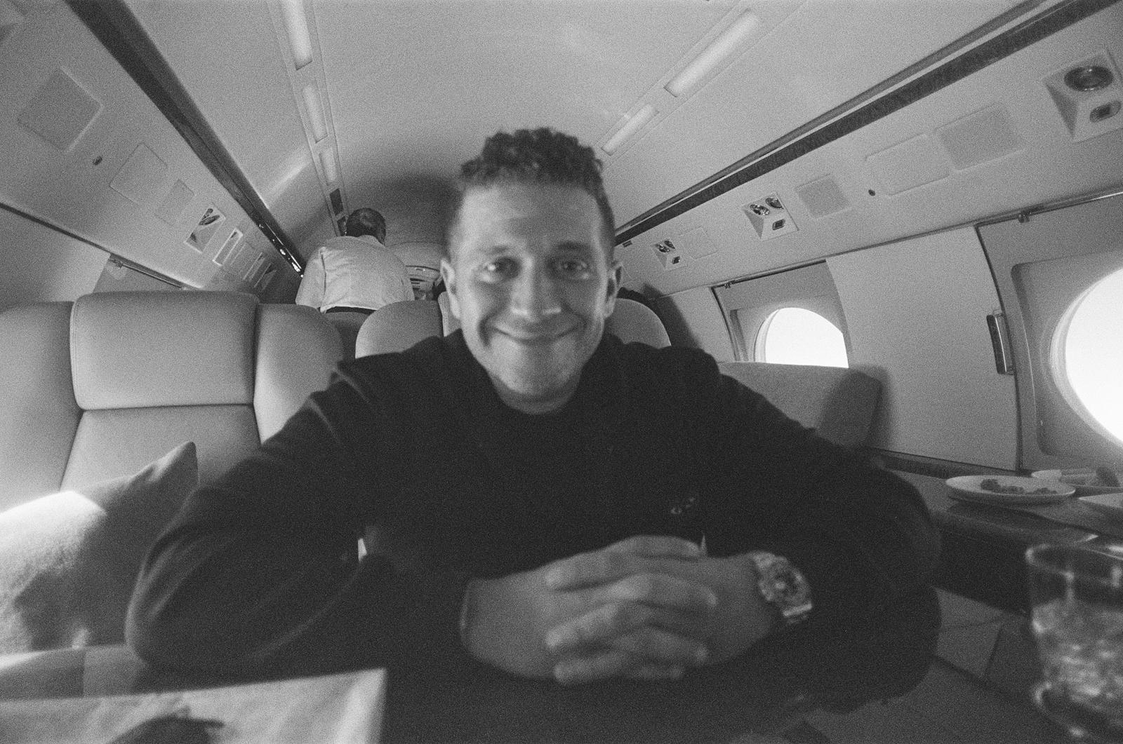 Jordan Fried smiling at a table aboard a private jet, photographed on black-and-white film